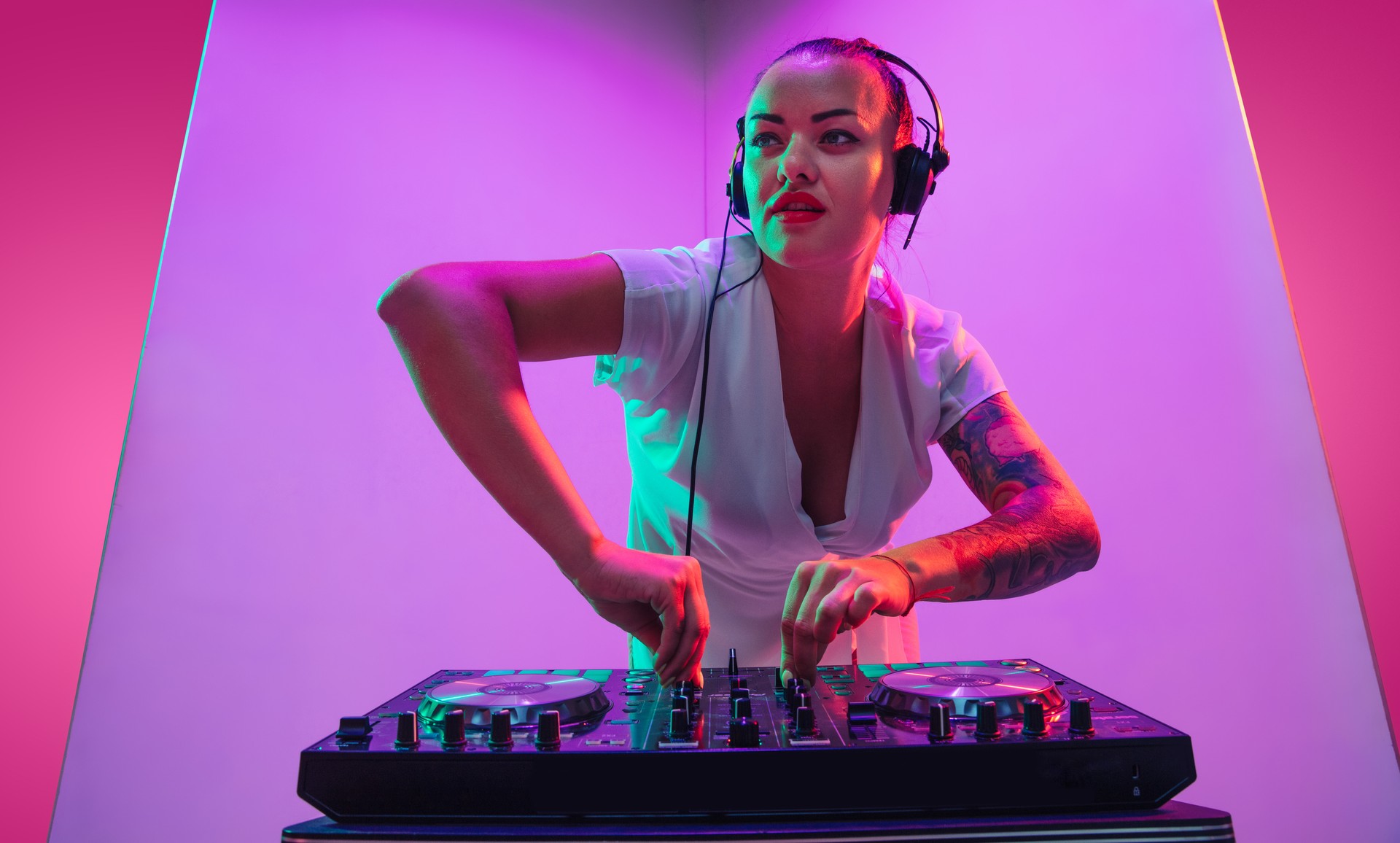 Young caucasian female musician in headphones performing on purple background in neon light